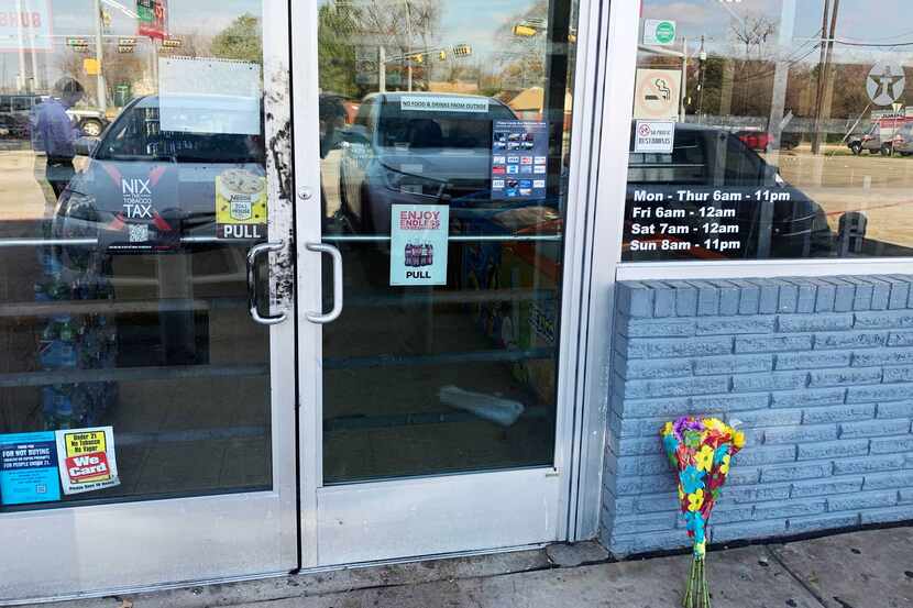 Flores yacen al pie de una tienda en una gasolinera de Texaco en Garland en donde tres...