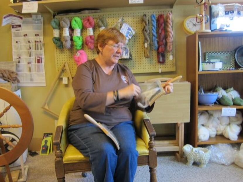 
Cindy Telisak cards wool by hand using flat wire paddle brushes in the Little Red Barn. The...