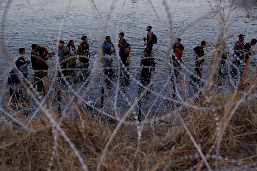 Migrants wait to climb over razor wire after crossing the Rio Grande and entering the U.S....