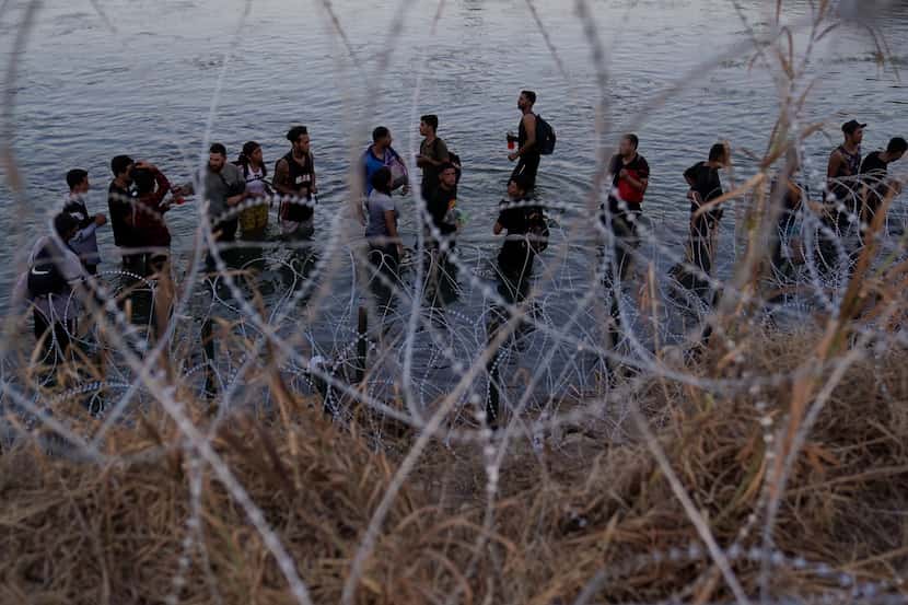 Migrants wait to climb over razor wire after crossing the Rio Grande and entering the U.S....