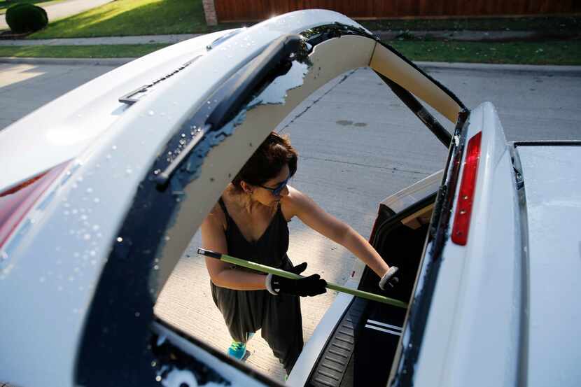 Genny Phillippe of Coppell works on cleaning broken glass from the back window of her...