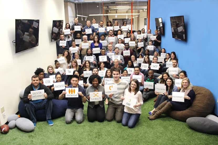 YourCause employees pose for a team photo. The cards represent things the company pledges to...