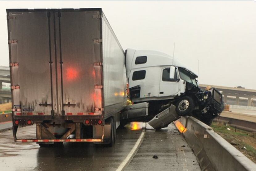 An 18-wheeler dangles over a concrete barrier on Interstate 635 after the truck jack-knifed...