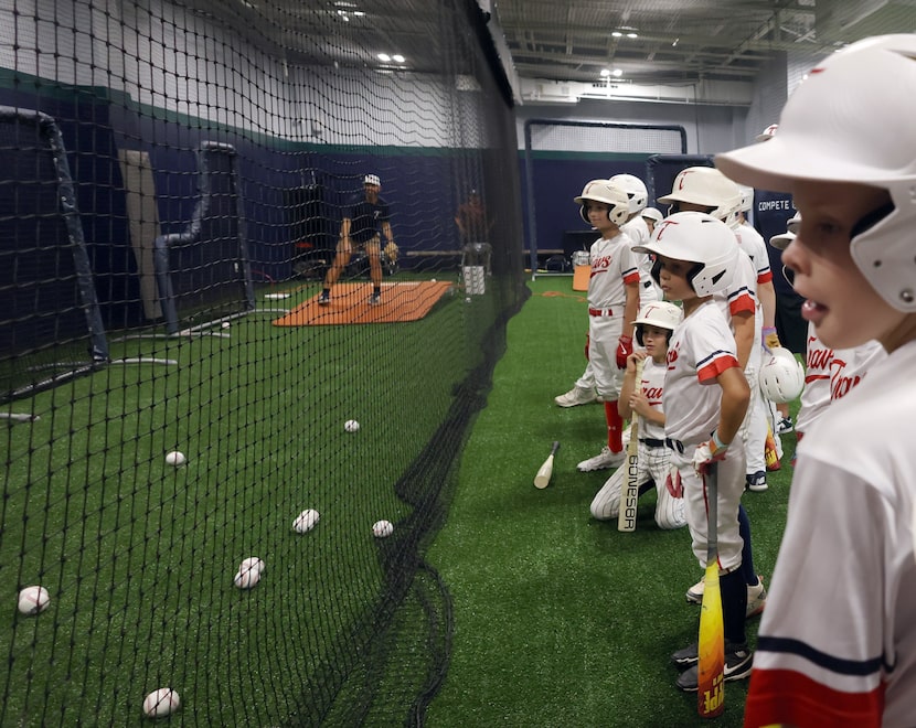 Members of the Travelers baseball team look on as a teammate finishes a batting cage session...