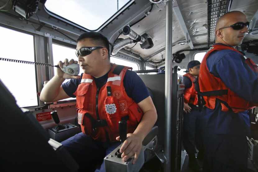 Coast Guard officer William Pless communicates on the radio while steering a Coast Guard...