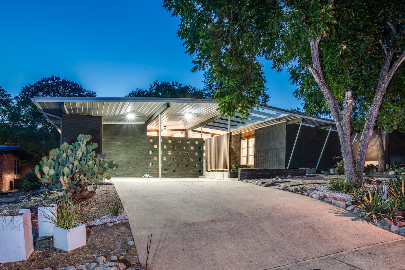 The home's green exterior features a cantilevered metal roof, decorative brick walls, and...