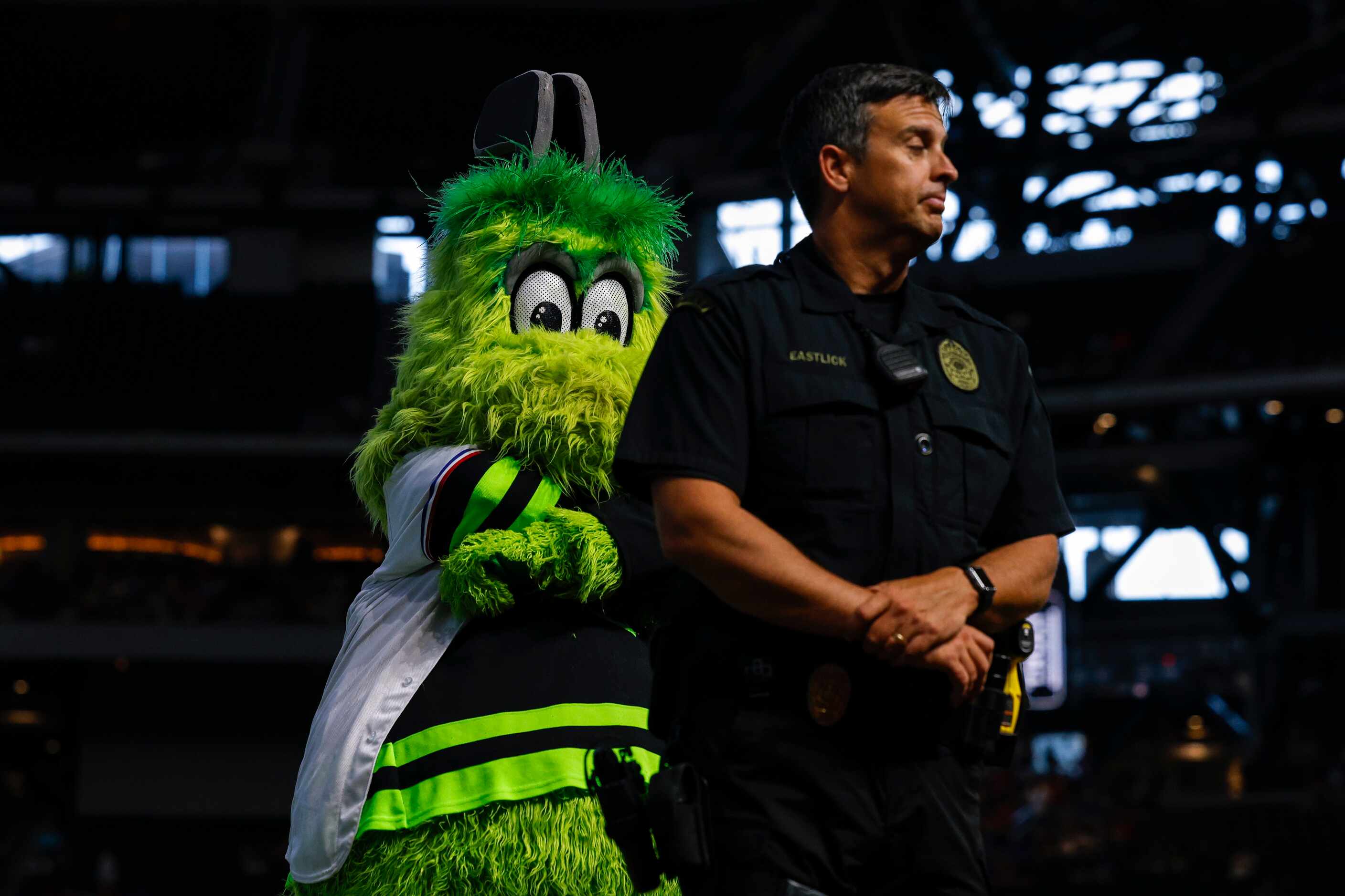 Dallas Stars mascot Victor E. Green looms behind an Arlington police officer before a...