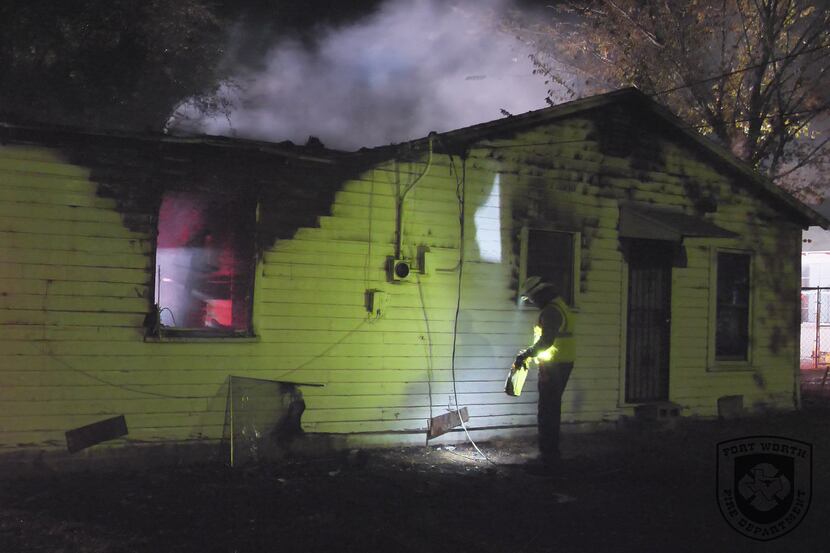A firefighter examines a home damaged by fire Wednesday morning in Fort Worth. One woman...