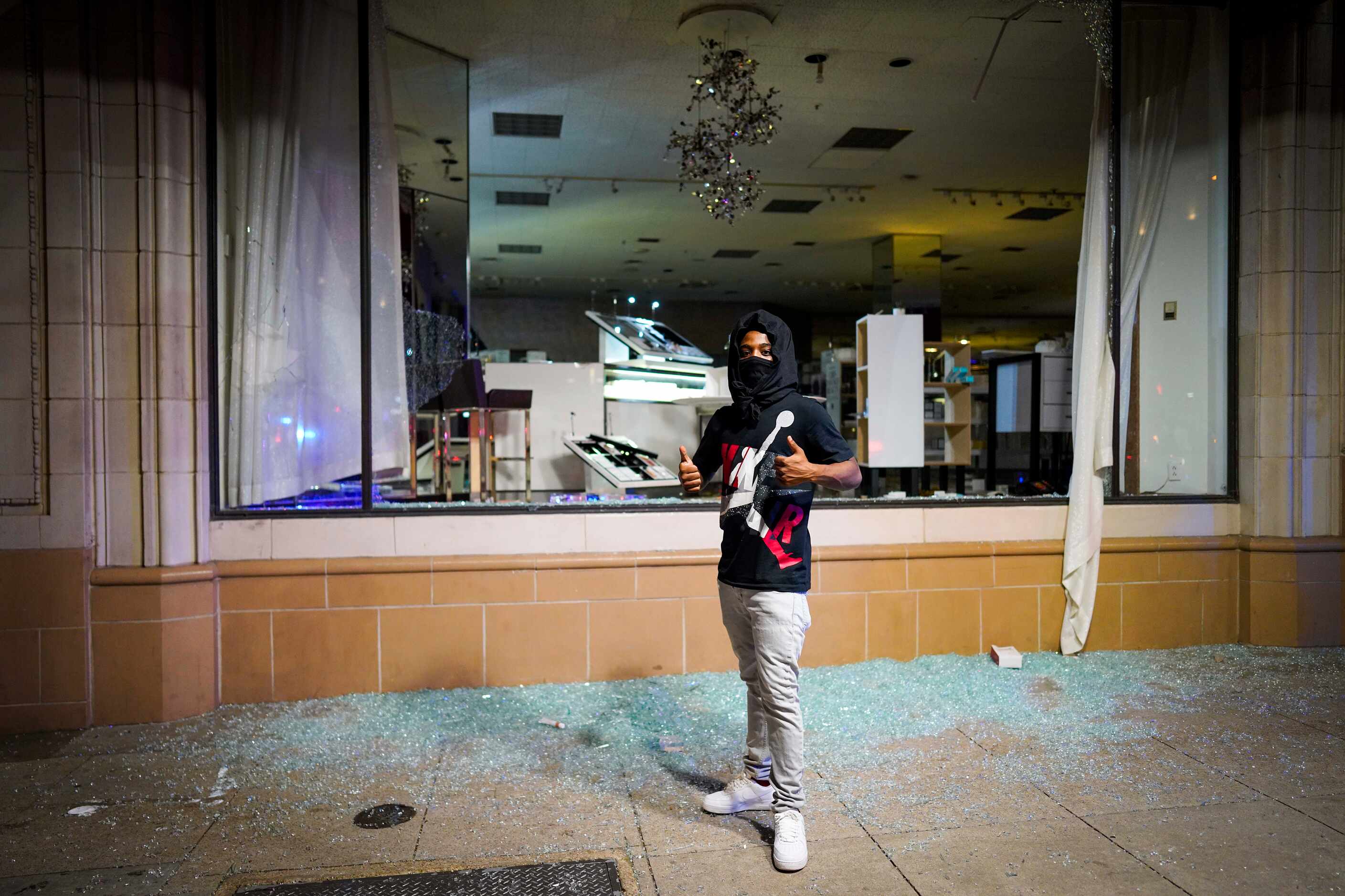 A man poses for a photo amidst broken glass after windows were smashed at the Nieman Marcus...