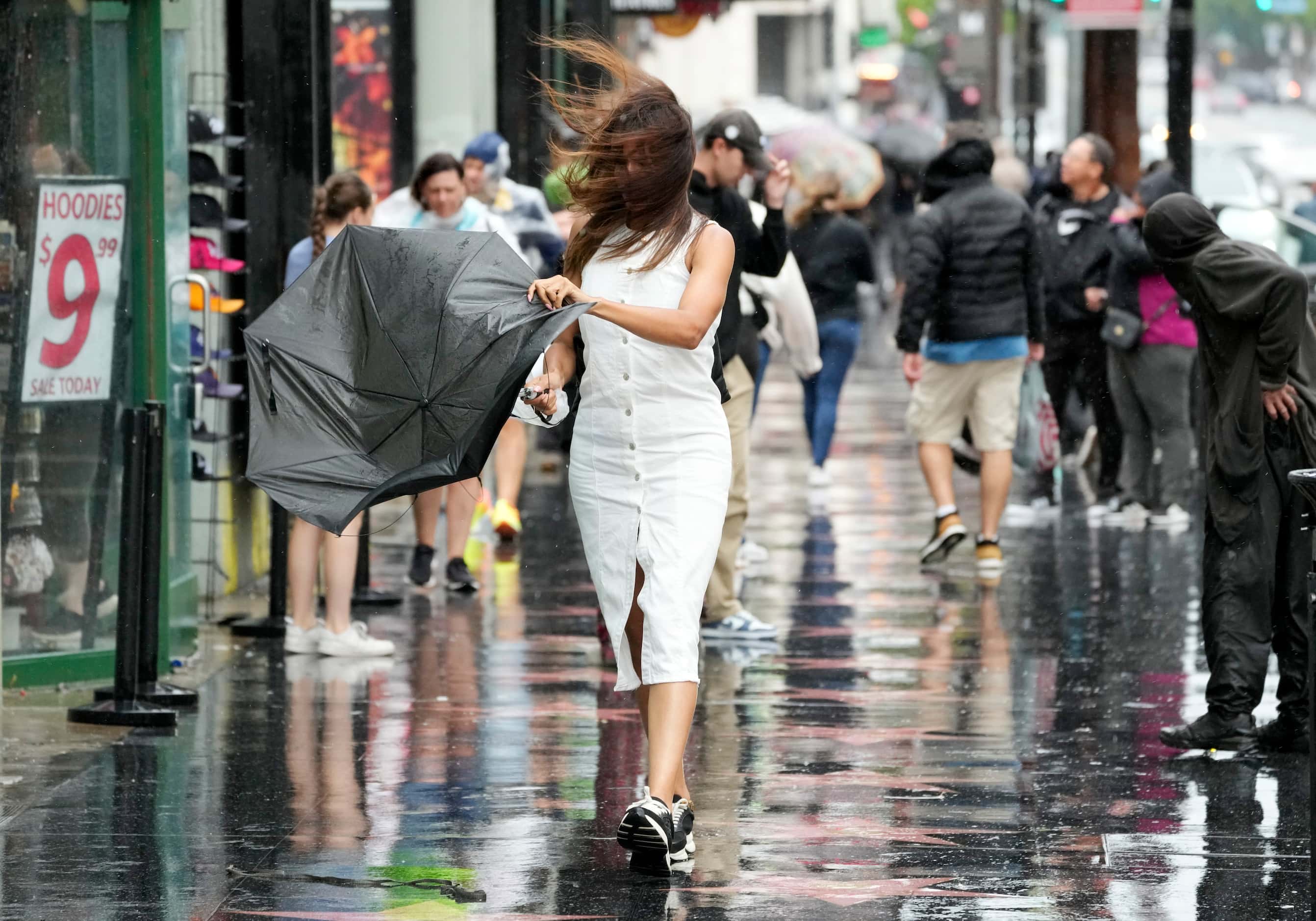 A pedestrian tends to a broken umbrella as she walks through wind and rain on Hollywood...