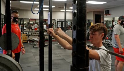 Coach Jared Hudgins (left) looks on as Brycen Alexander does a squat routine during the day...