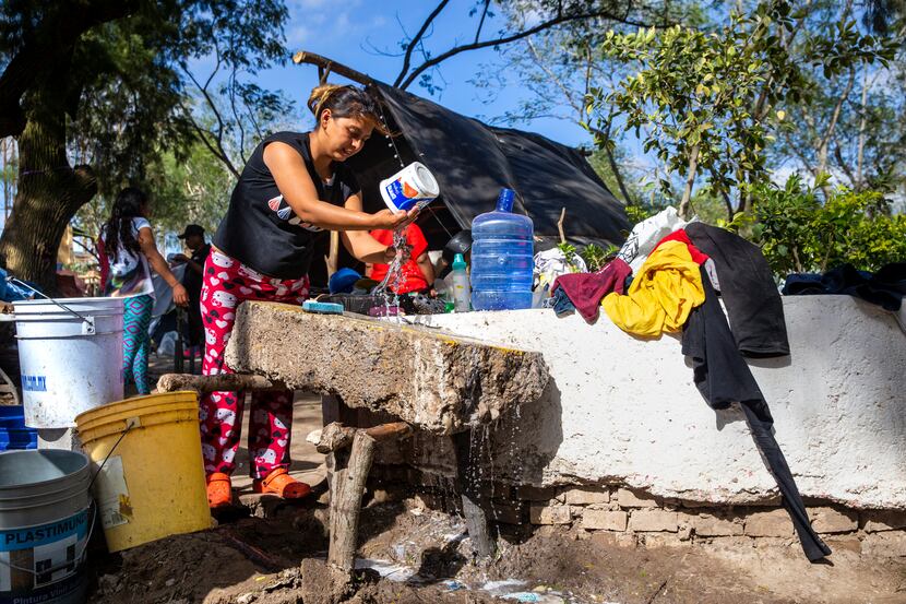 Alejandra Perez, an asylum-seeker from Honduras, washes dishes with water from buckets at...