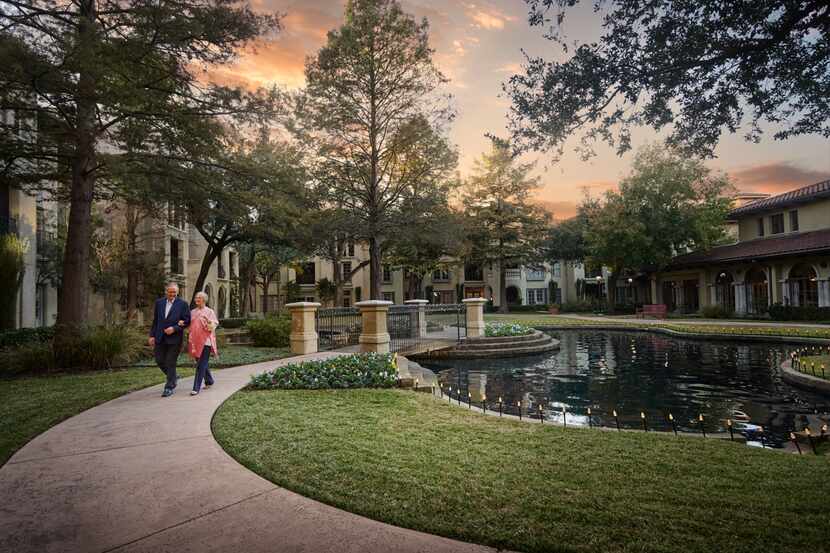 Wide shot of a landscaped outdoor courtyard with a couple walking along a paved path around...
