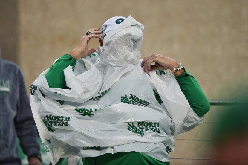 A North Texas Mean Green fan fights against the wind as he tries to put on a poncho in the...