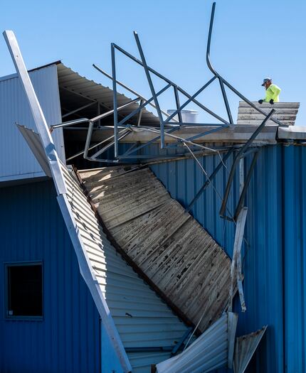 Workers clear sheet metal from the roof of Polymer Products in Grand Prairie, which suffered...