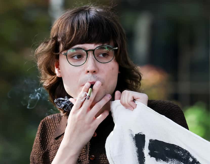 Maxine Davis inhales smoke while holding the corner of a “Decrim Denton” banner in front of...