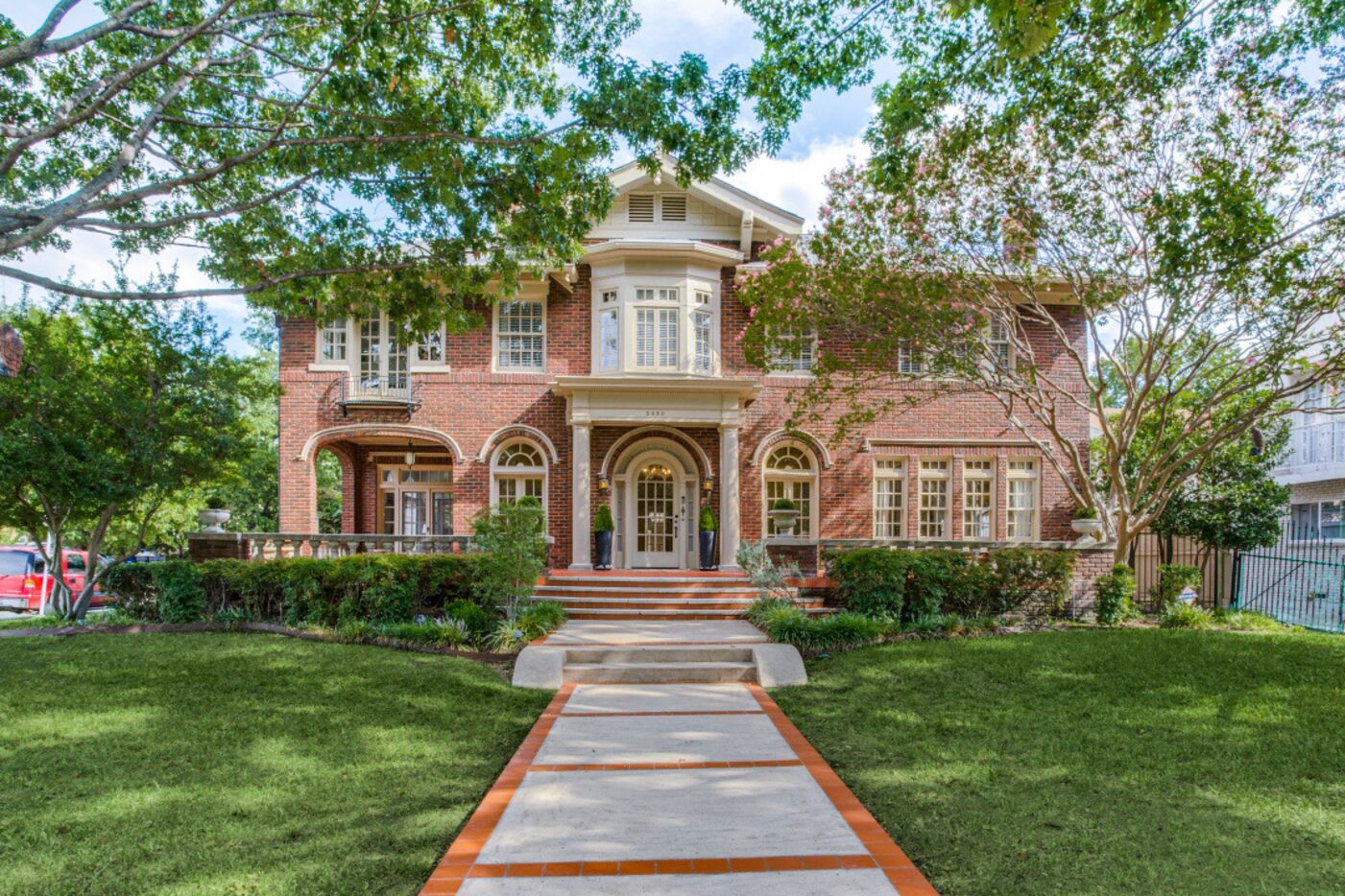 A large Georgian style home with red brick sits on a large yard.