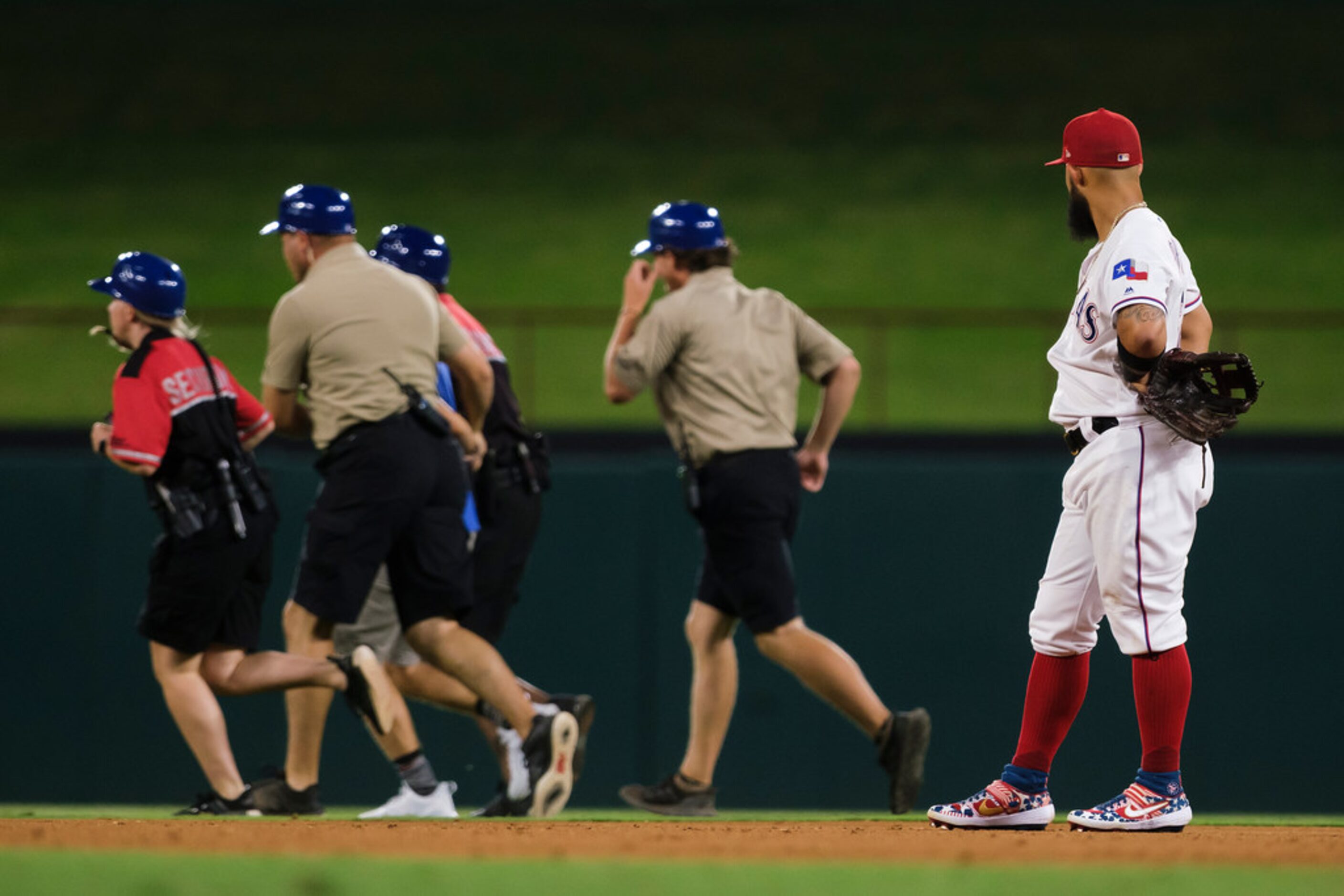 Texas Rangers second baseman Rougned Odor watches as security guards remove a fan who ran on...