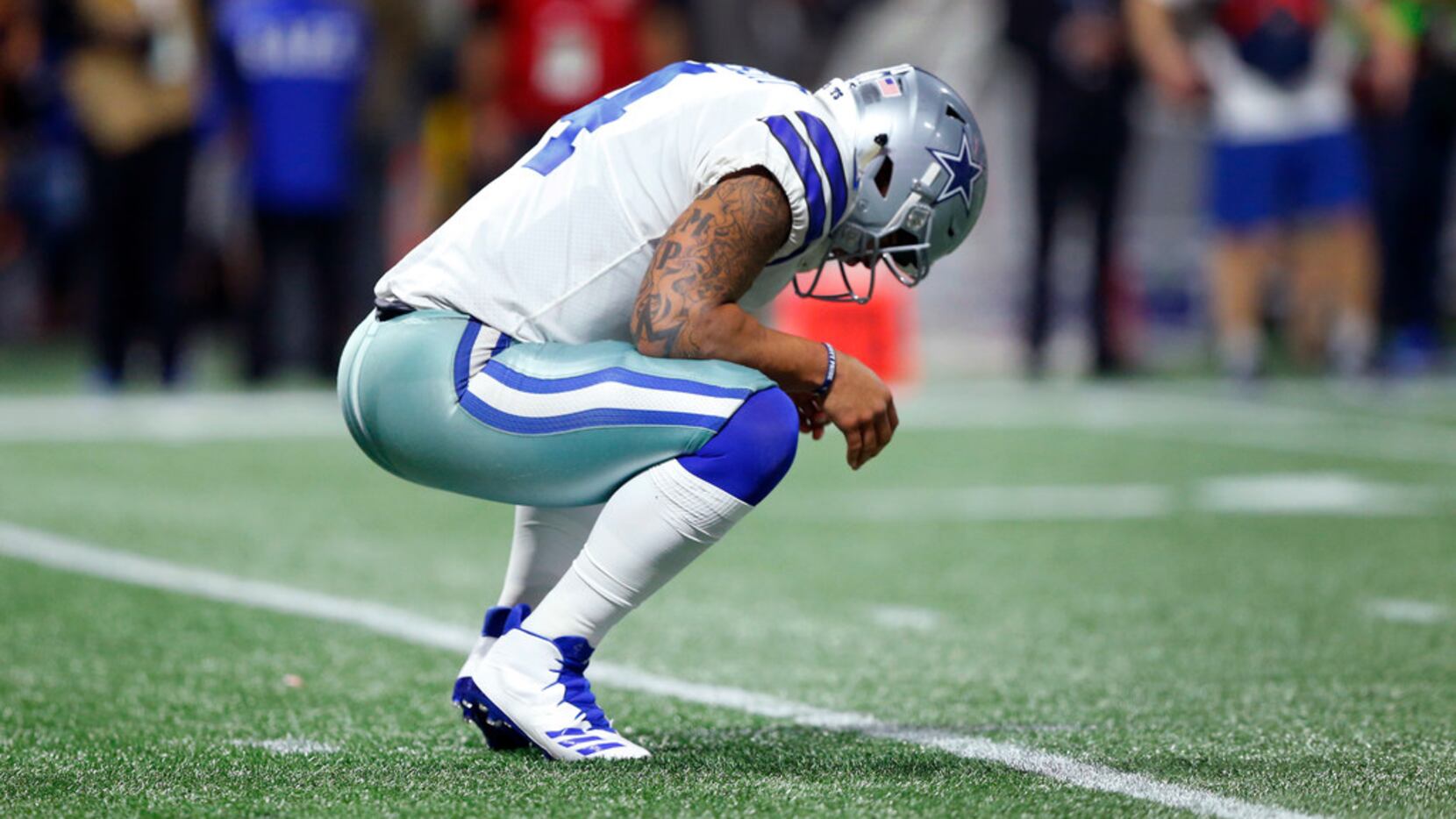 Dallas Cowboys quarterback Dak Prescott (4) squats on the field to stretch his back after...