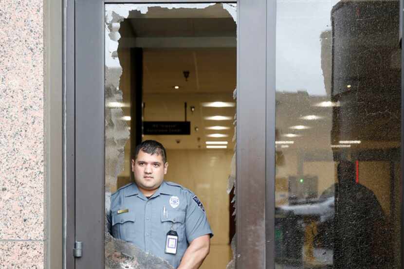 A security officer looks out from shattered glass after shots were fired Monday morning,...