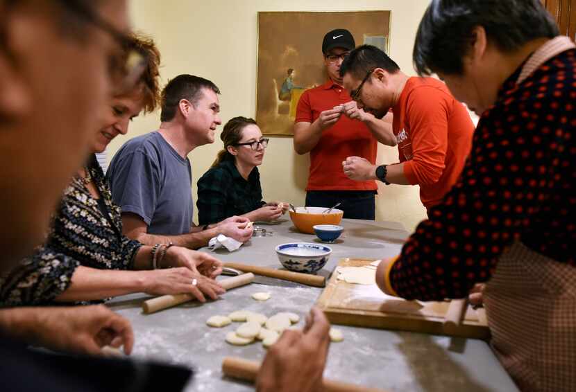 A group of friends and family, led by Lin Wang (top-right) work on forming Chinese dumplings...