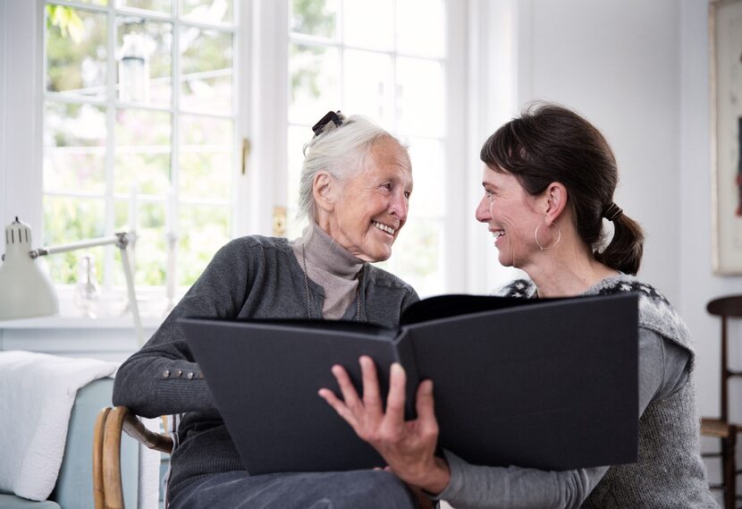 Elder mother and younger daughter smile at each other while looking through photo album.