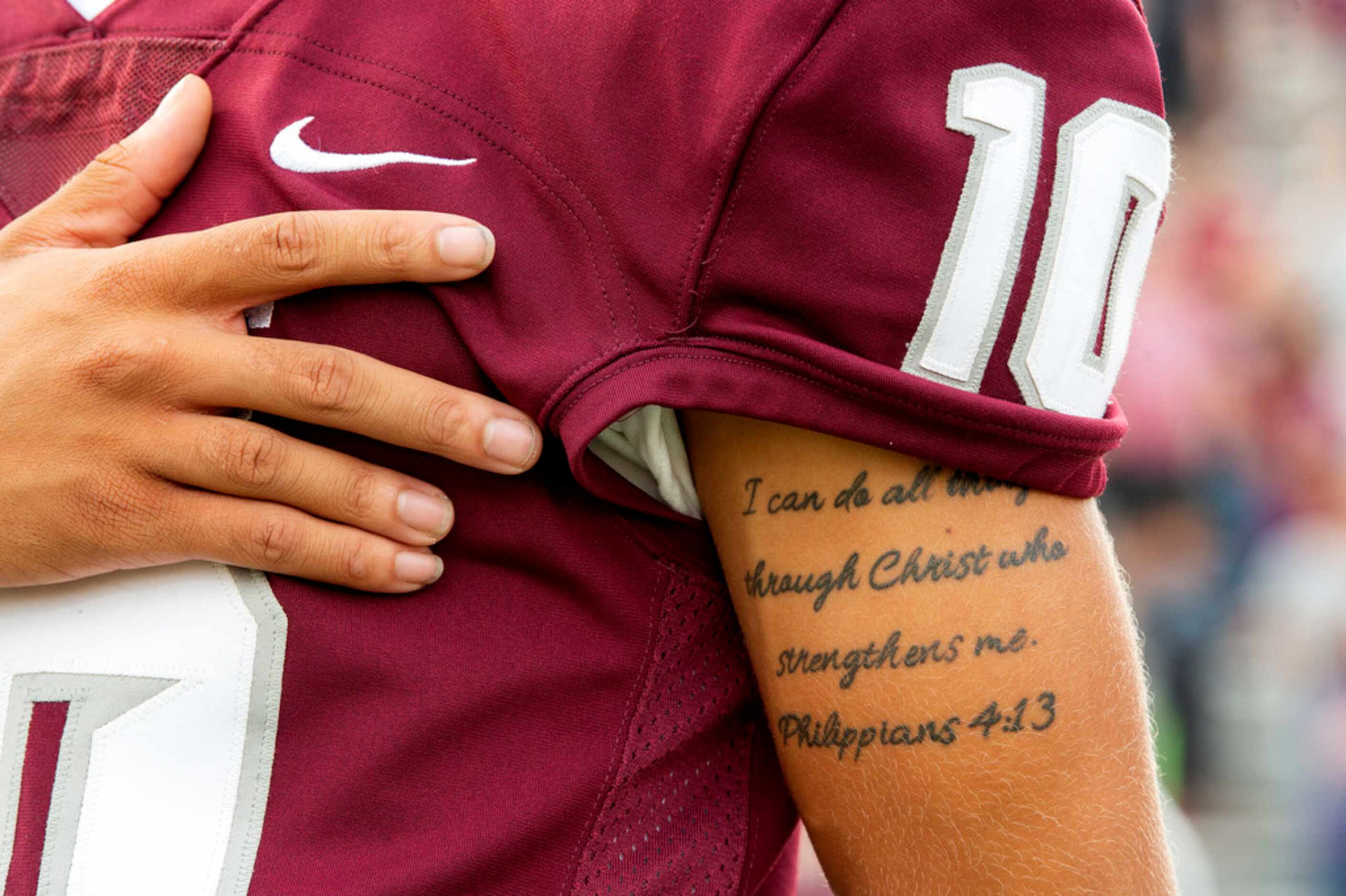 Lewisville senior EJ Hister's arm bears a biblical tattoo as he stands at attention for the...