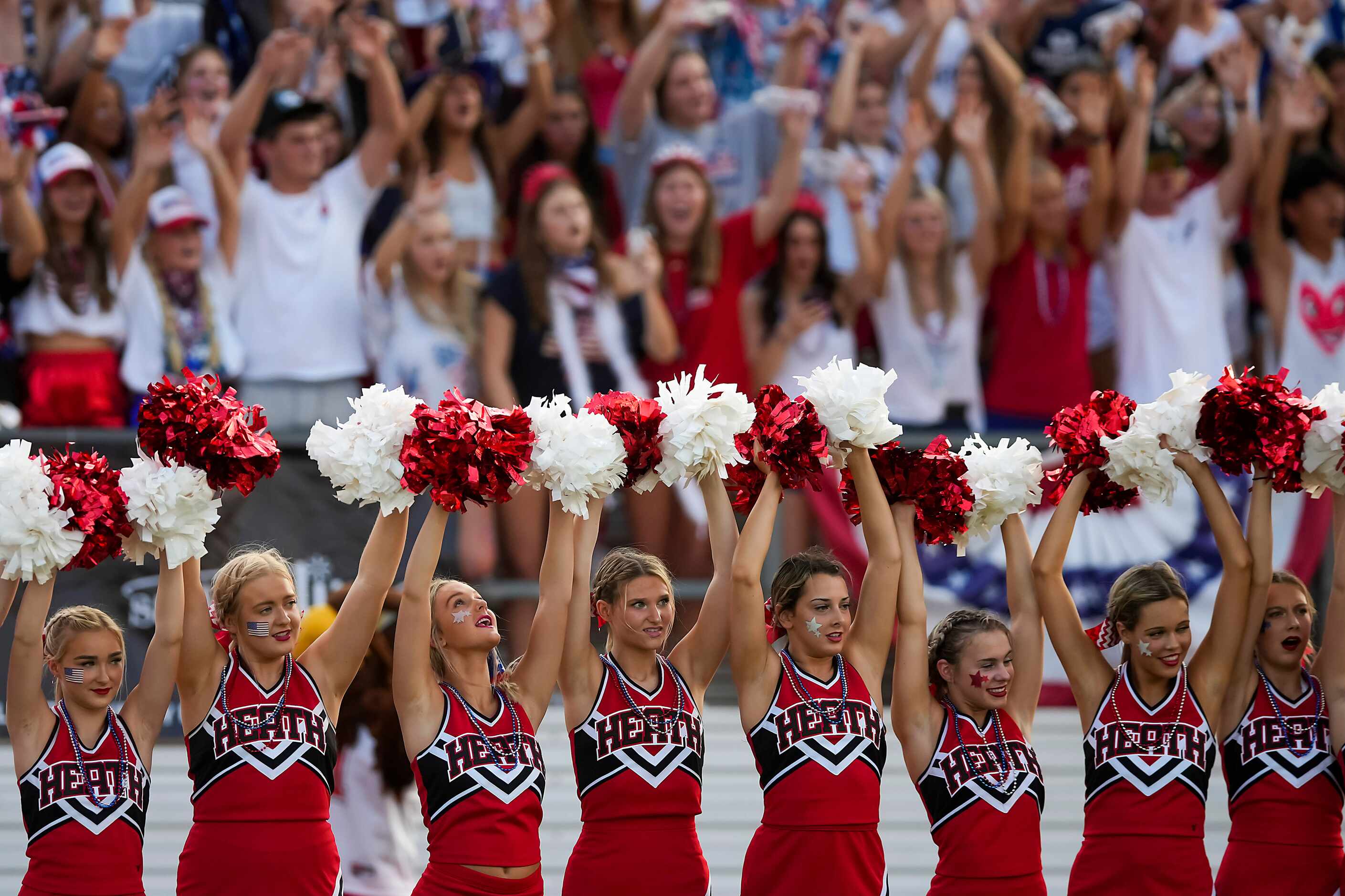 Rockwall-Heath cheerleaders raise their arms for the opening kickoff of a high school...