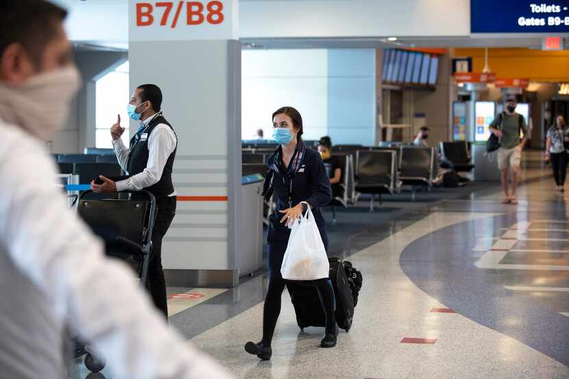 A flight attendant wearing a face-covering walks the concourse with her bags in Terminal B...