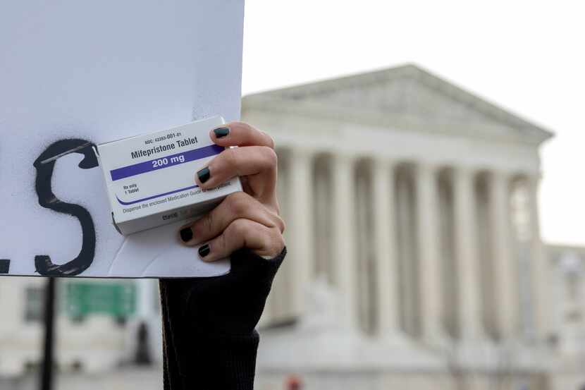 An abortion-rights activist holds a box of mifepristone pills as demonstrators from...