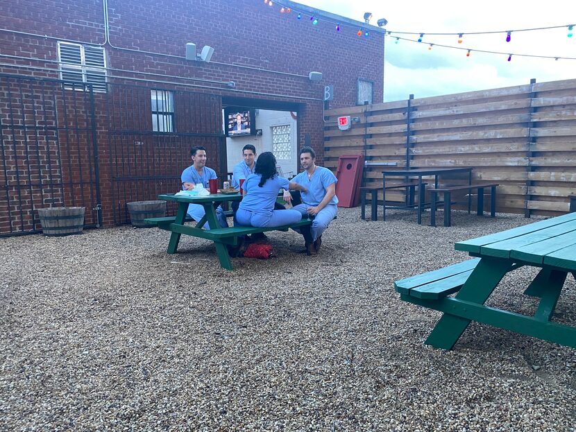 A table of customers in scrubs relaxed with drinks outdoors at Redfield's Tavern in Dallas'...