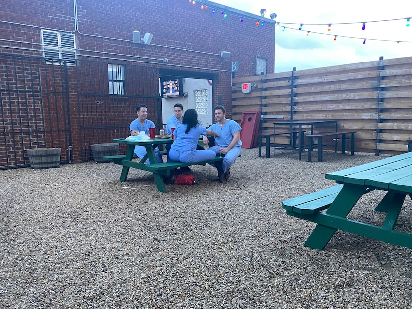 A table of customers in scrubs relaxed with drinks outdoors at Redfield's Tavern in Dallas'...
