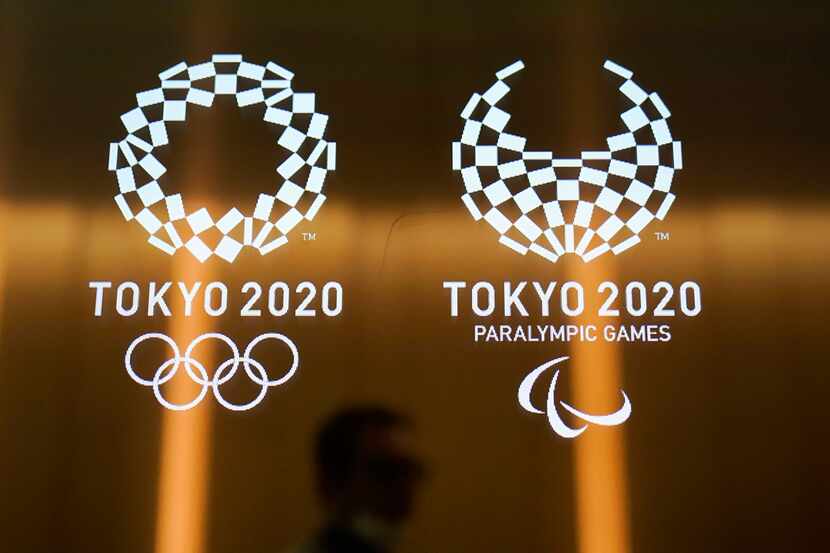 FILE - In this June 11, 2019, file photo, a man walks past the logos of the Tokyo 2020...