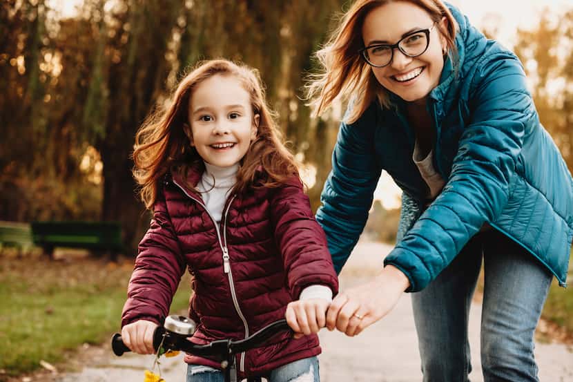 Girl learning how to ride a bicycle with her mother laughing in the park.