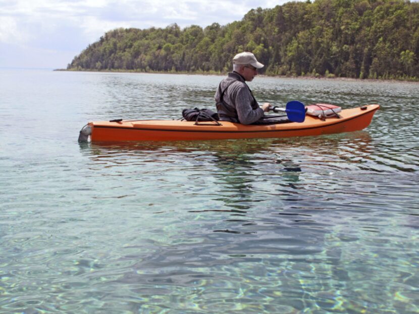 A kayaker pauses to contemplate a shipwreck below in the shallow waters of Grand Traverse Bay.