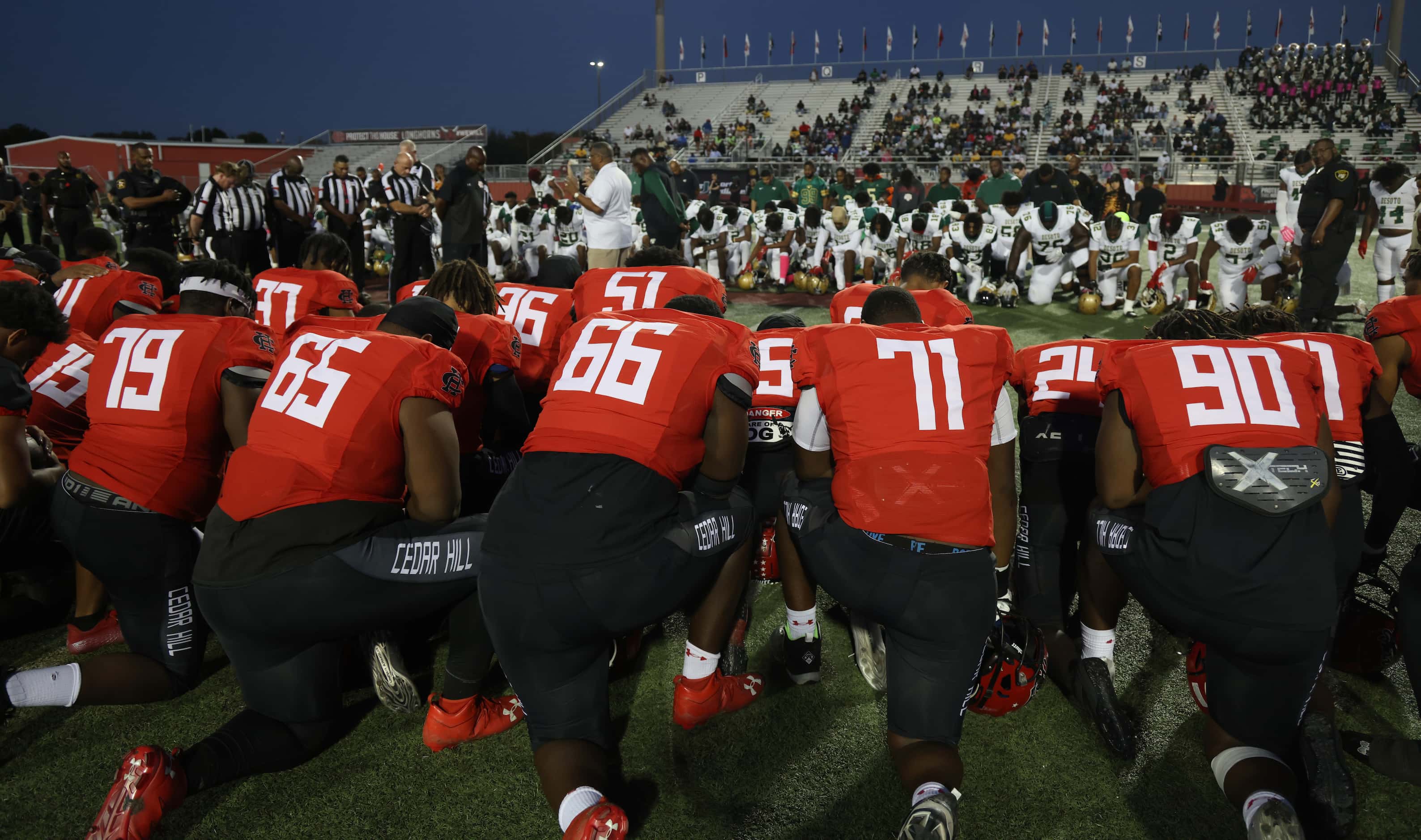 Members of the Cedar Hill and DeSoto football teams take a knee during a prayer at midfield...