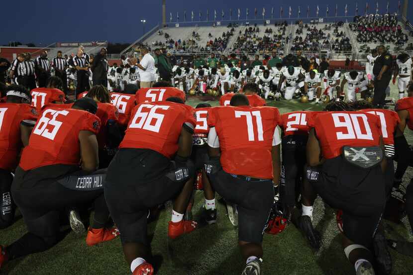 Members of the Cedar Hill and DeSoto football teams take a knee during a prayer at midfield...