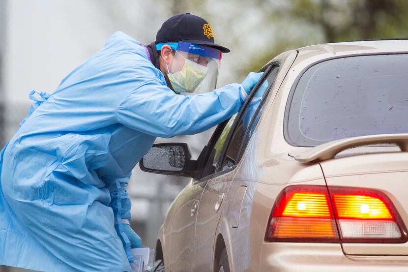 A medical professional takes a patient's temperature before letting them into a testing site...