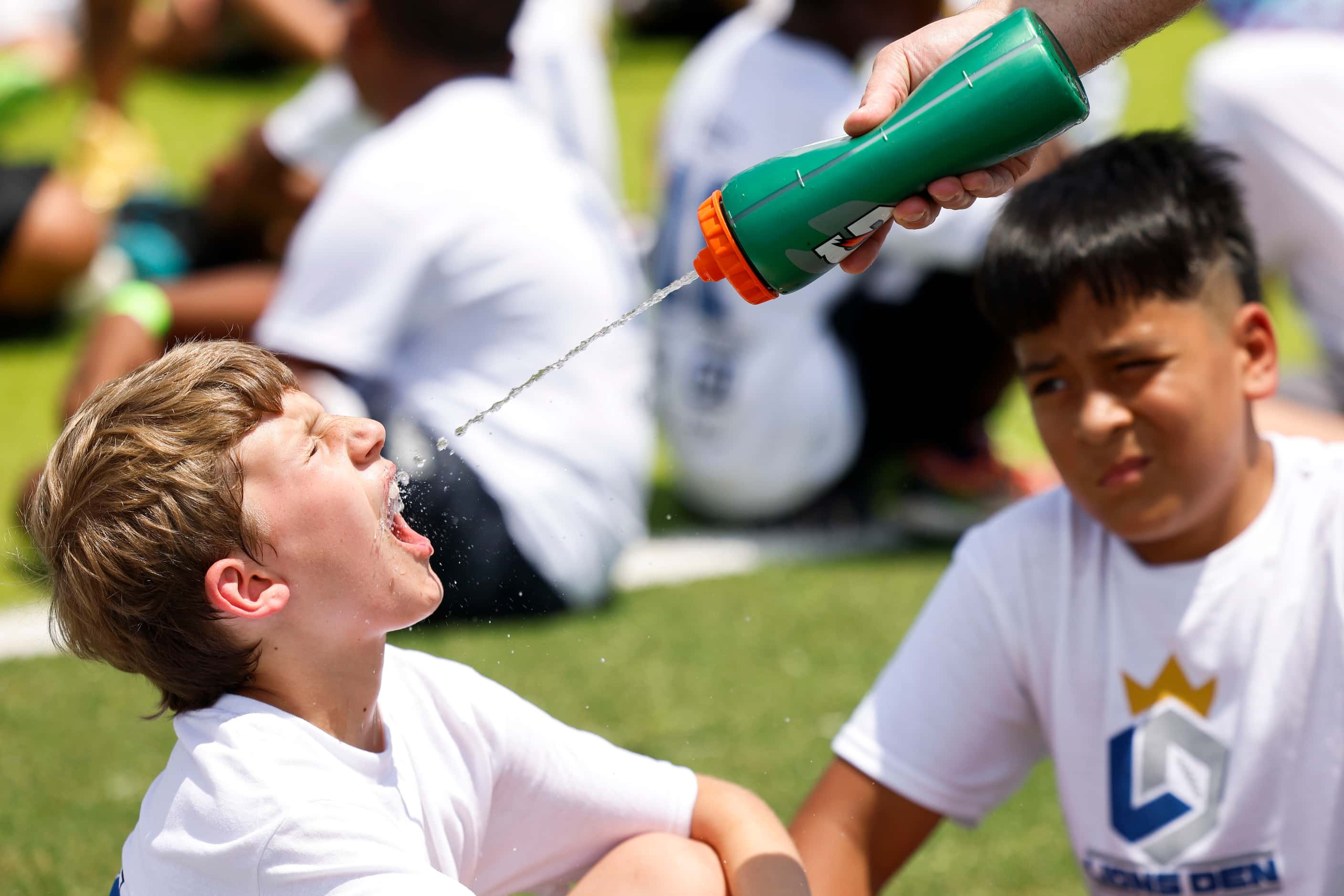Oliver Clayton, 9, (left) gets a sip of water as Ivan Ramirez follows while lining up to...