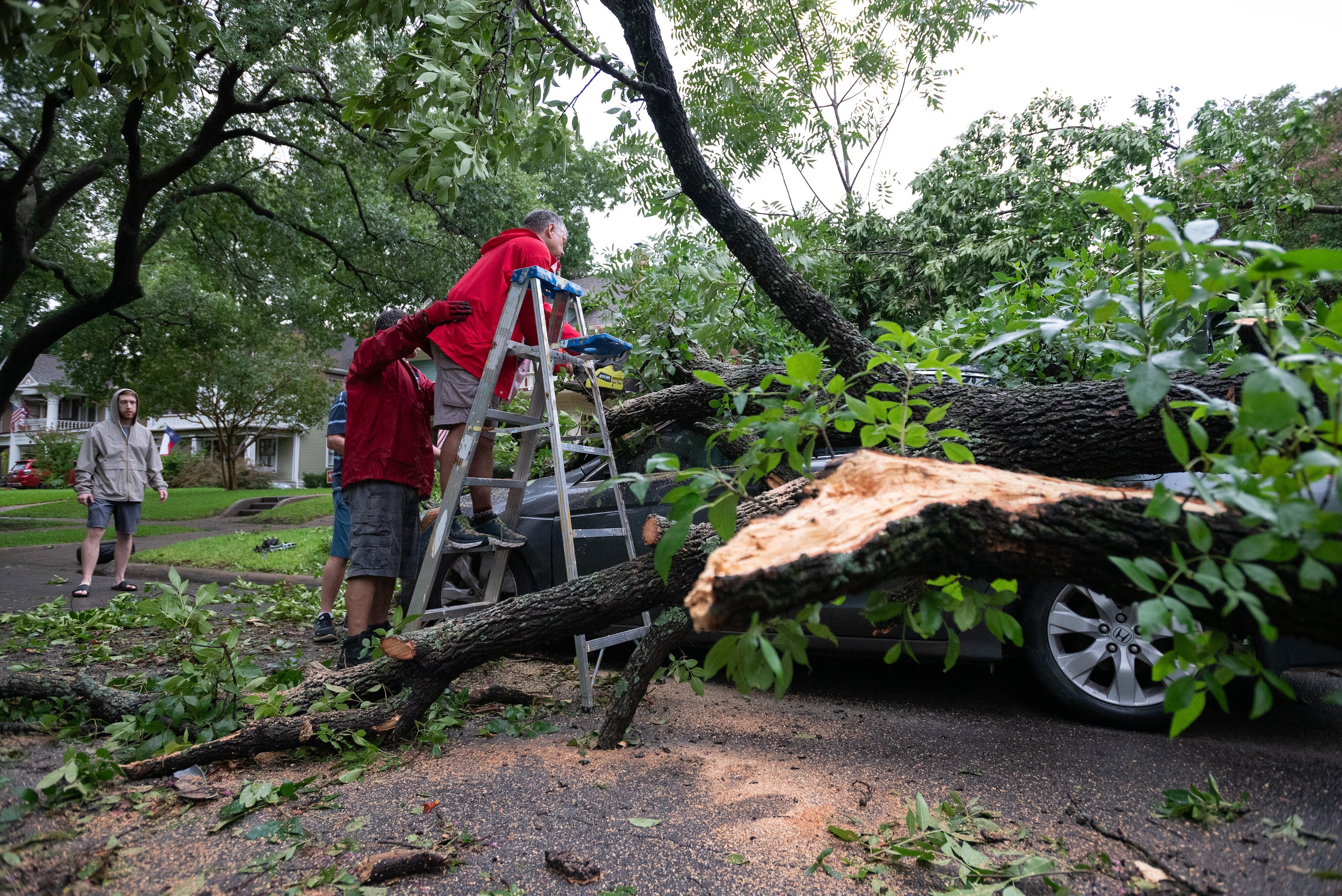 Mark Guest, 55, stands on a ladder with the help of neighbor Eric Warheit, 51, as Guest uses...