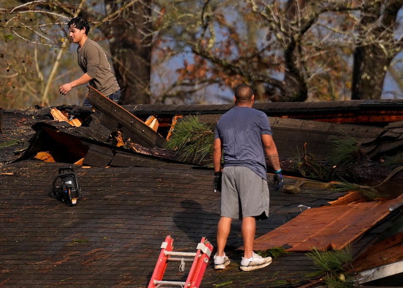 Men work to remove debris and cover a damaged roof after strong thunderstorms pass through...