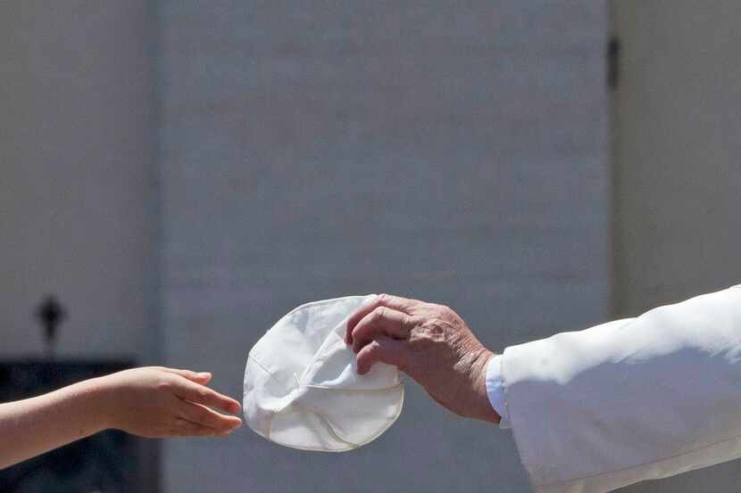 
Pope Francis (right) handed his skull cap to a child in exchange for one she donated to...