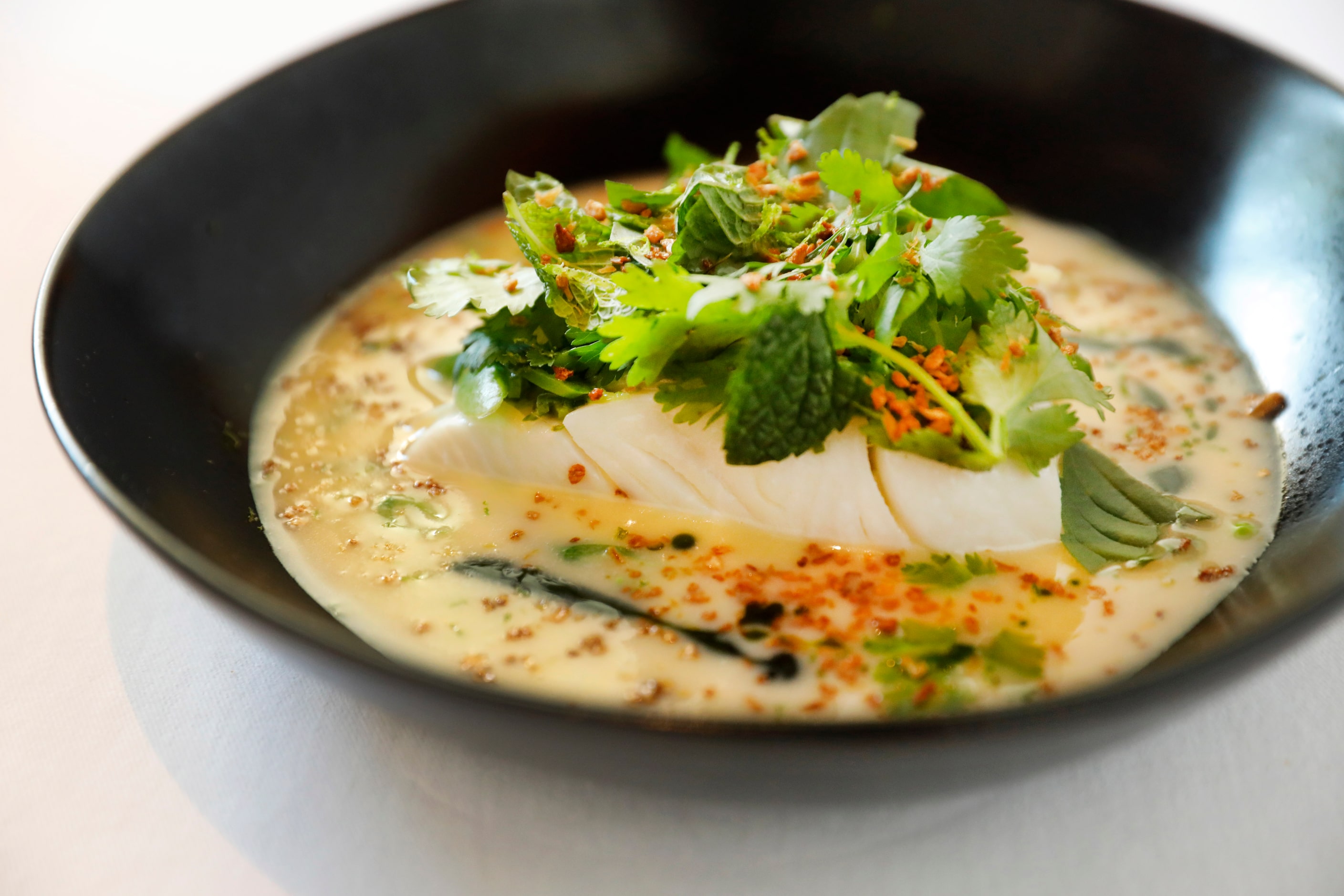 Steamed halibut is prepared with ginger beurre blanc, Thai herbs and snap peas at Le...