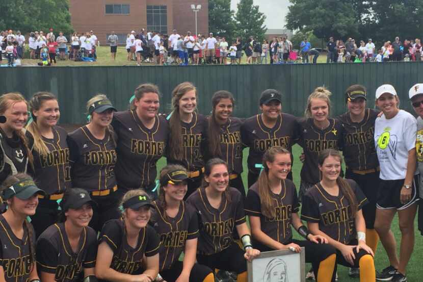The Forney softball team poses for pictures after Saturday's game while holding a picture of...