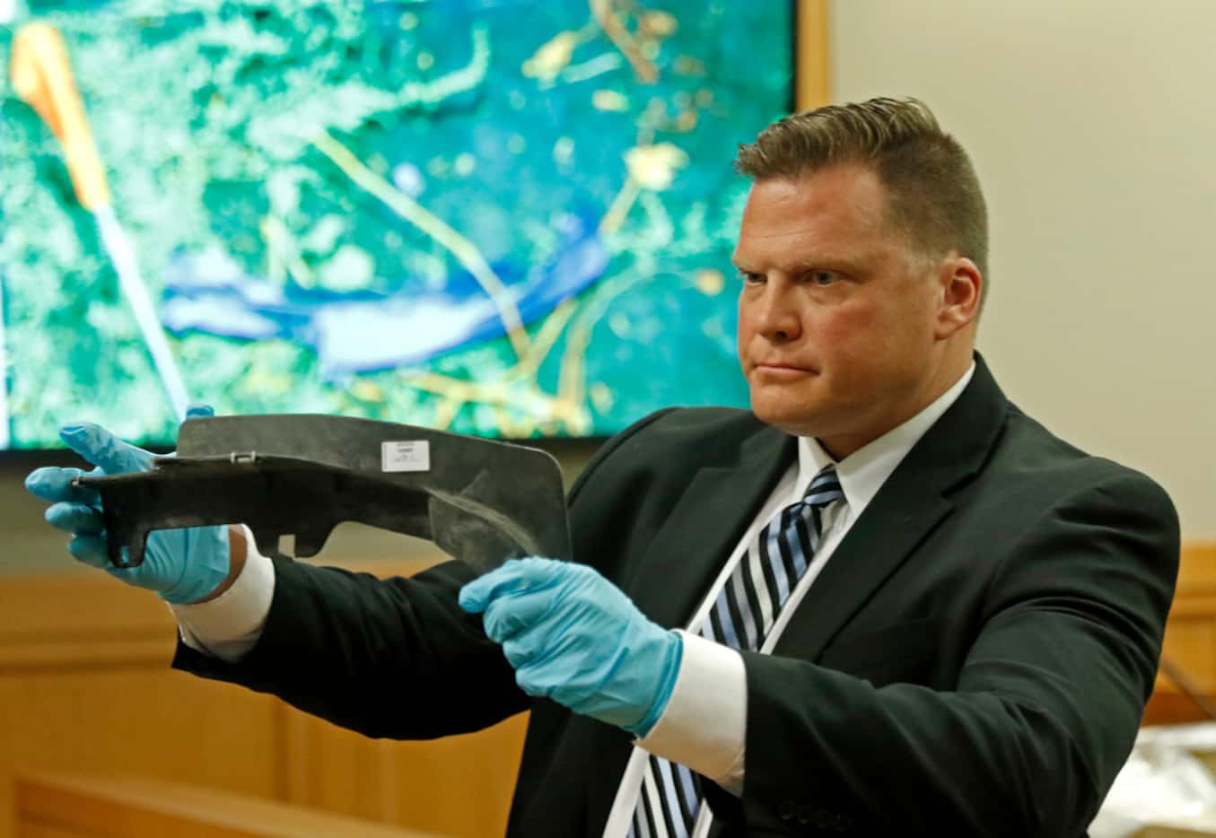 Richardson Detective Eric Willadsen shows the jury an auto part found at the crime scene in...