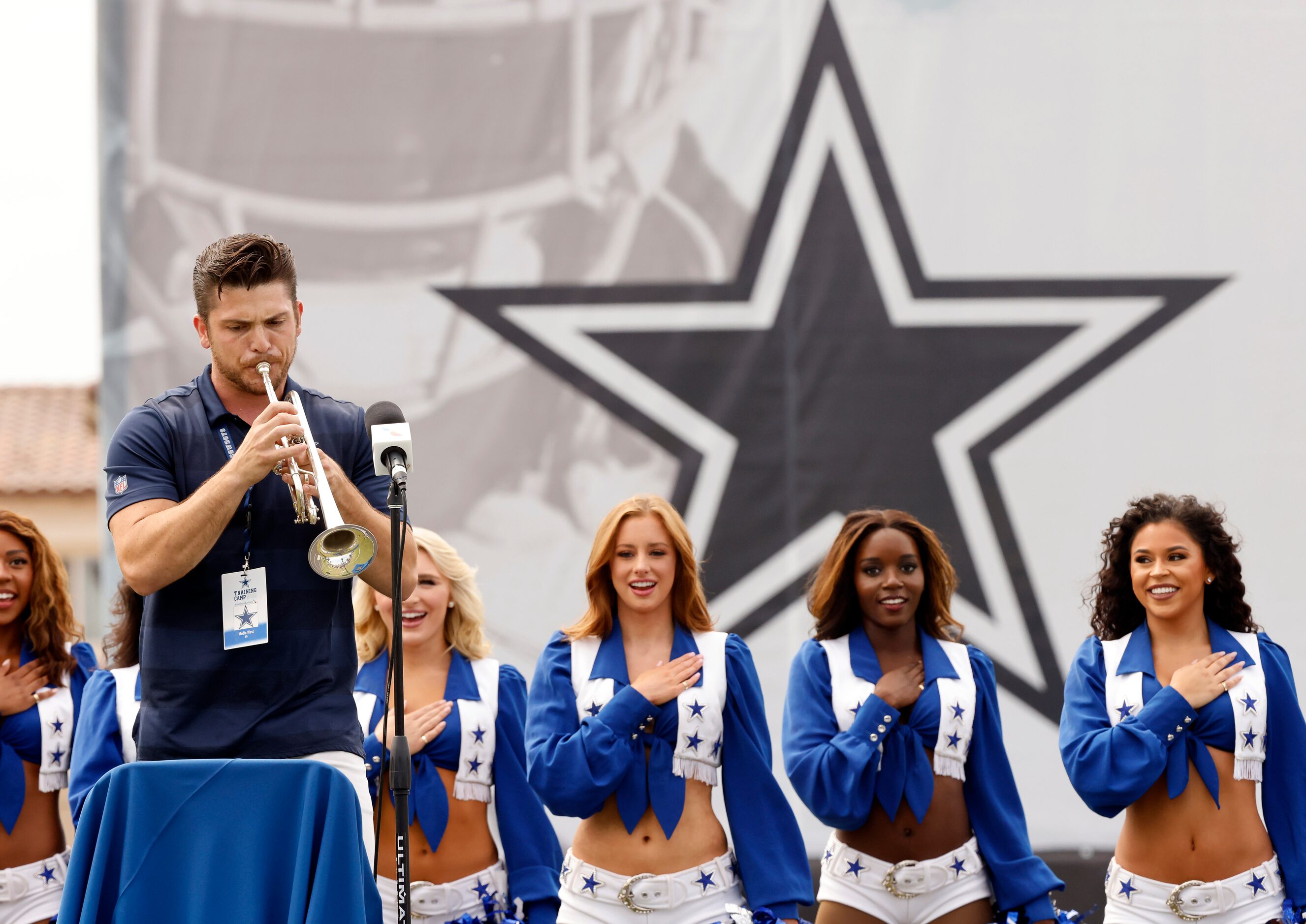 The the background of Dallas Cowboys Cheerleaders, trumpeter Bryce Schmidt performs the...