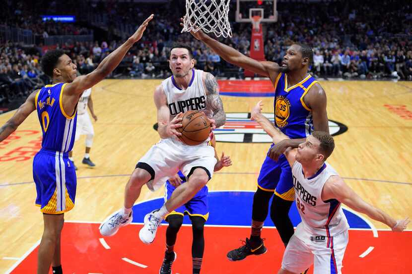 El guardia de los Clippers de Los Ángeles, J.J. Redick, pasa por en medio de dos jugadores...