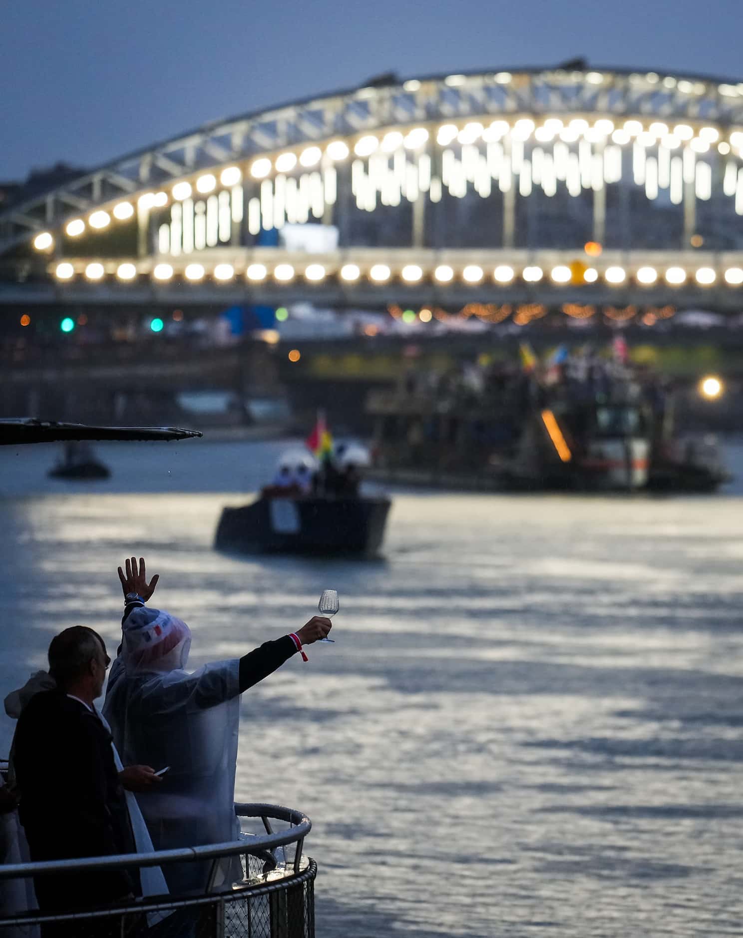 A spectator raises a glass of wine while cheering boats passing along the Seine with athlete...