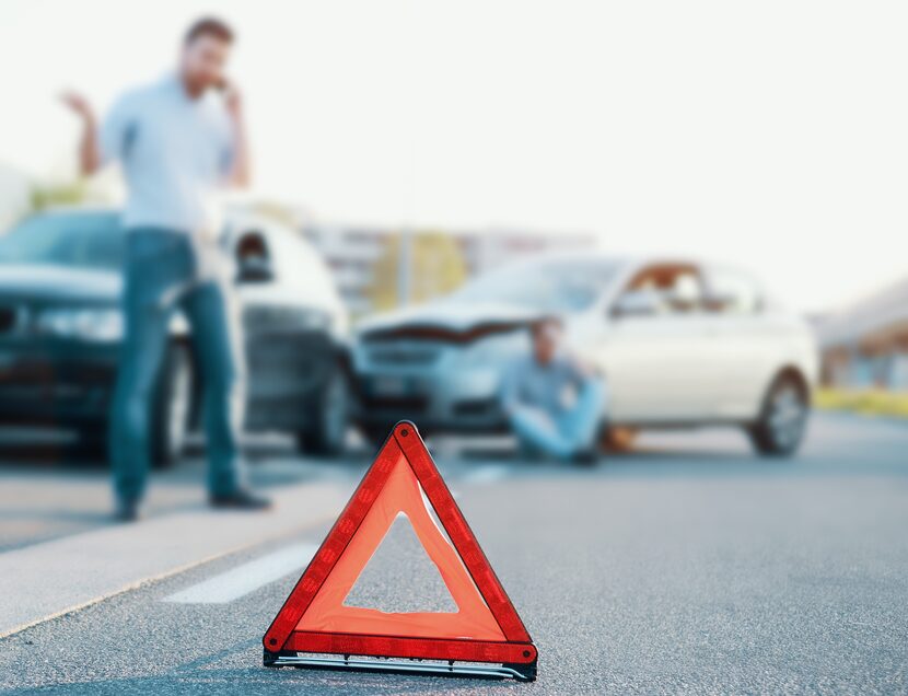 Man calling first aid after a bad car crash on the road, main focus on red triangle