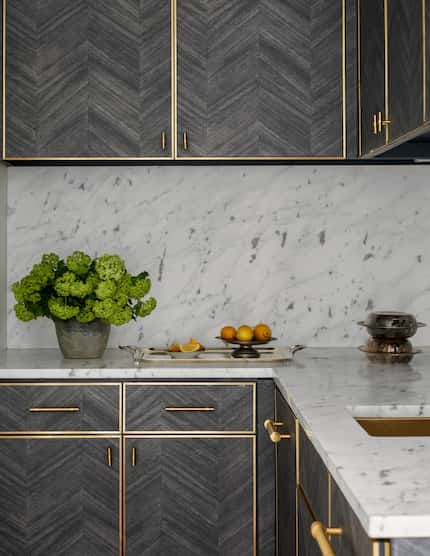 Cabinets with a chevron pattern have brass accents. Marble covers the countertop and the...